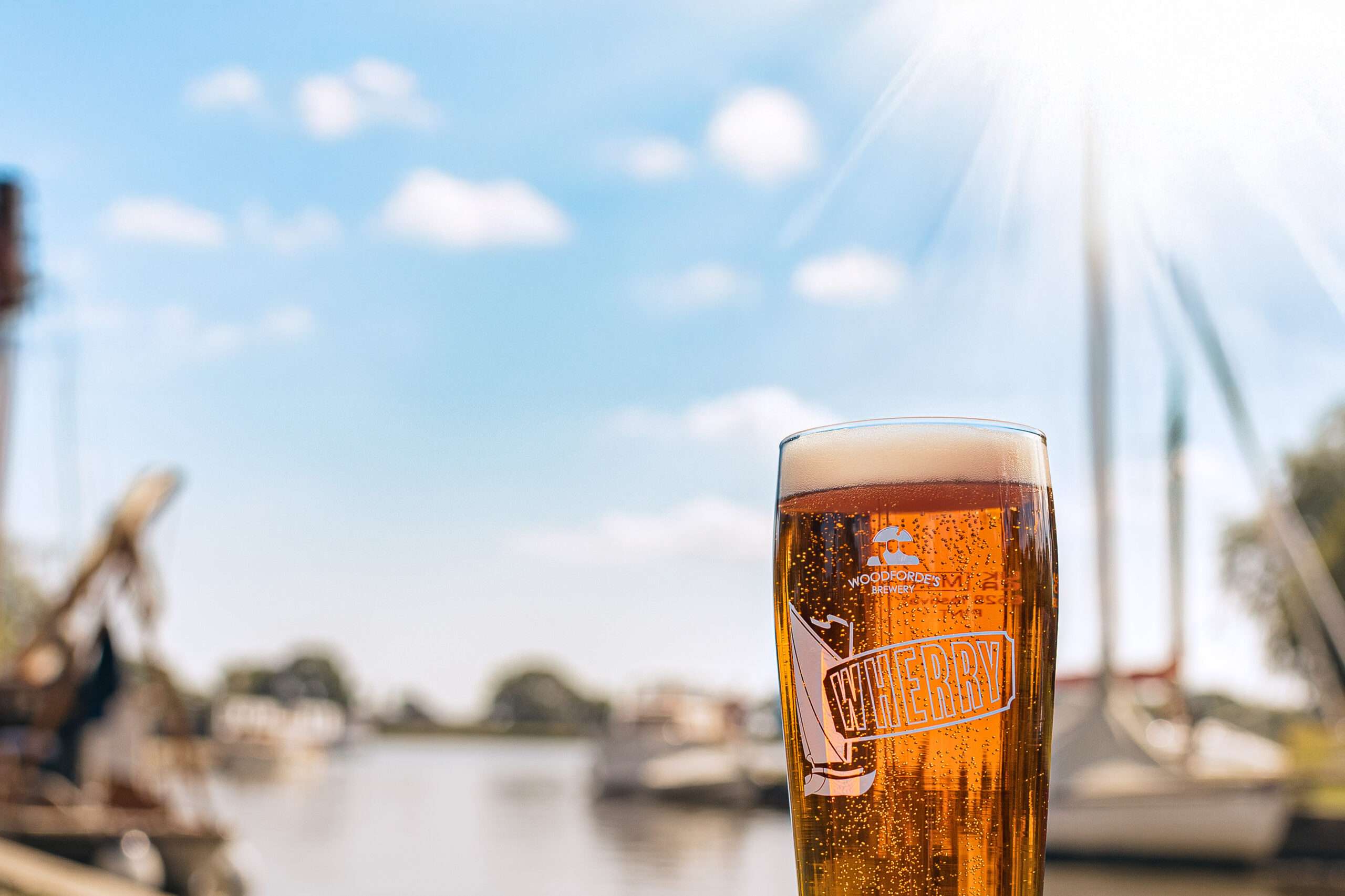 A pint of Woodforde’s Wherry ale served outdoors, showcasing the brewery’s award-winning beer against a bright blue sky.