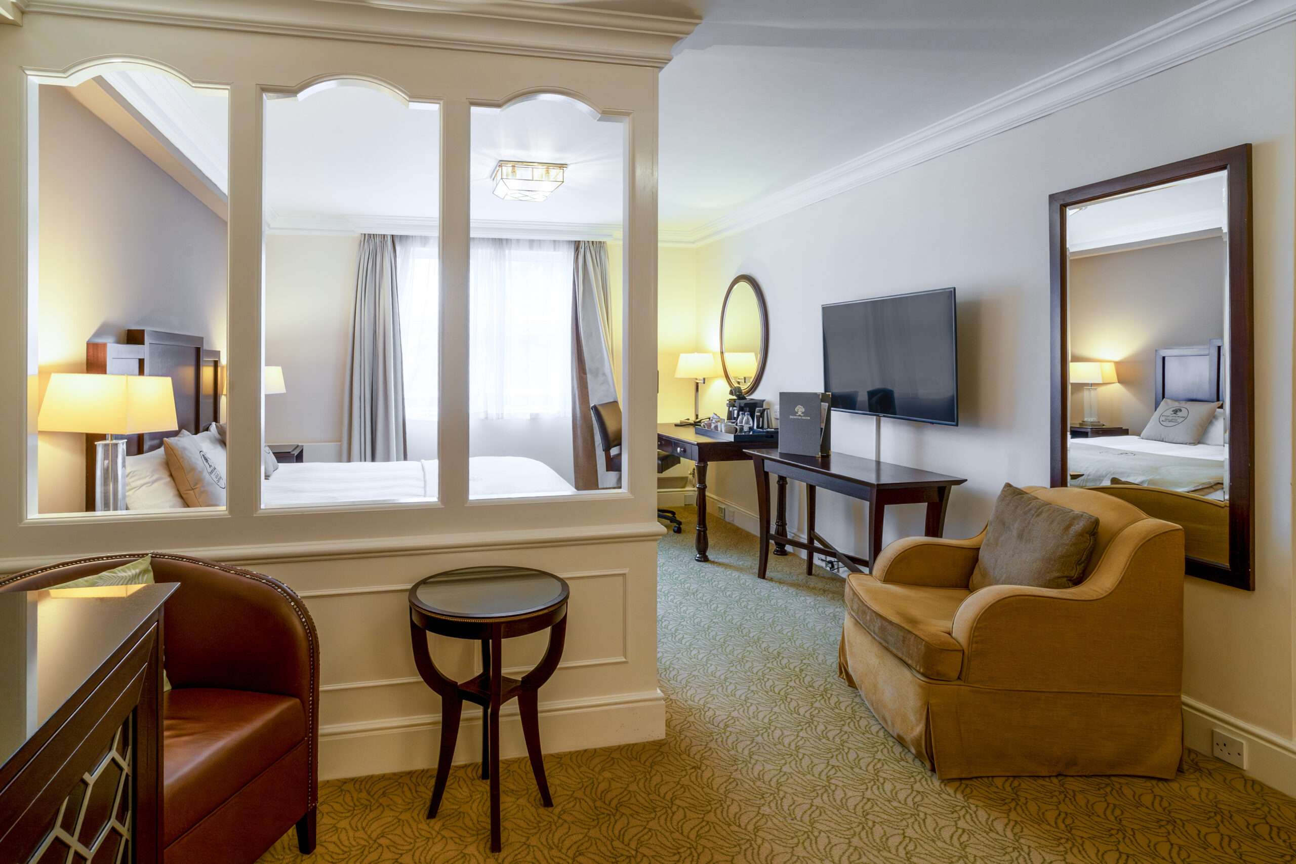 Spacious hotel bedroom at Sprowston Manor Hotel with large mirror, seating area and modern furnishings.