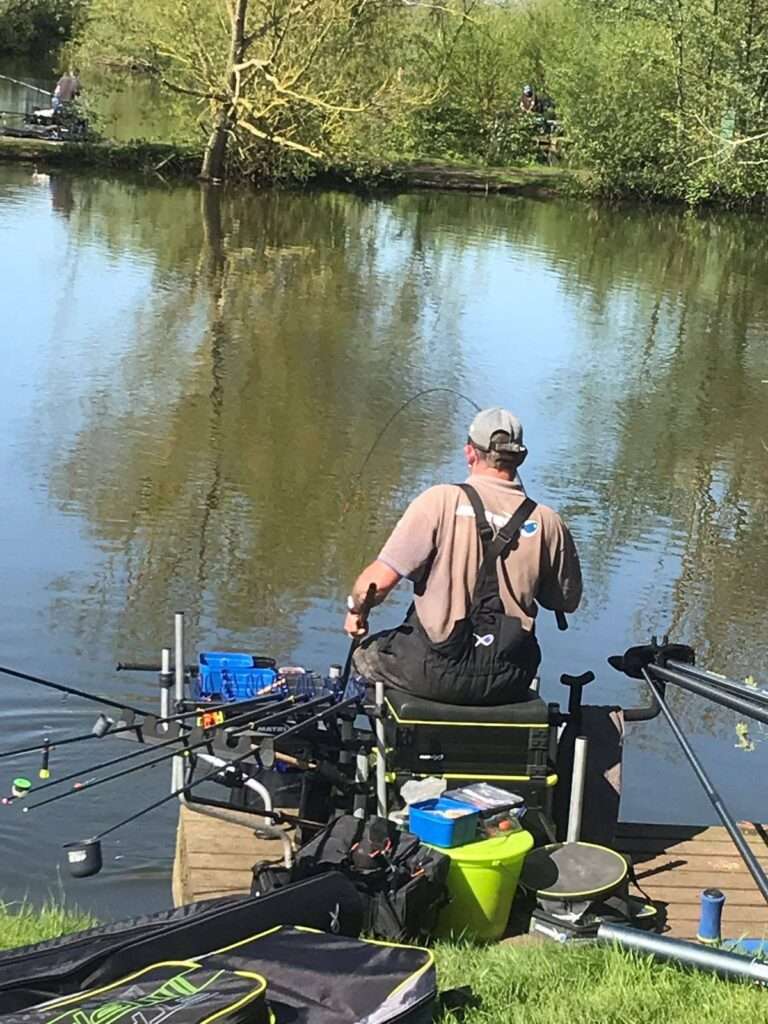 Angler fishing beside a calm Norfolk waterway surrounded by nature.