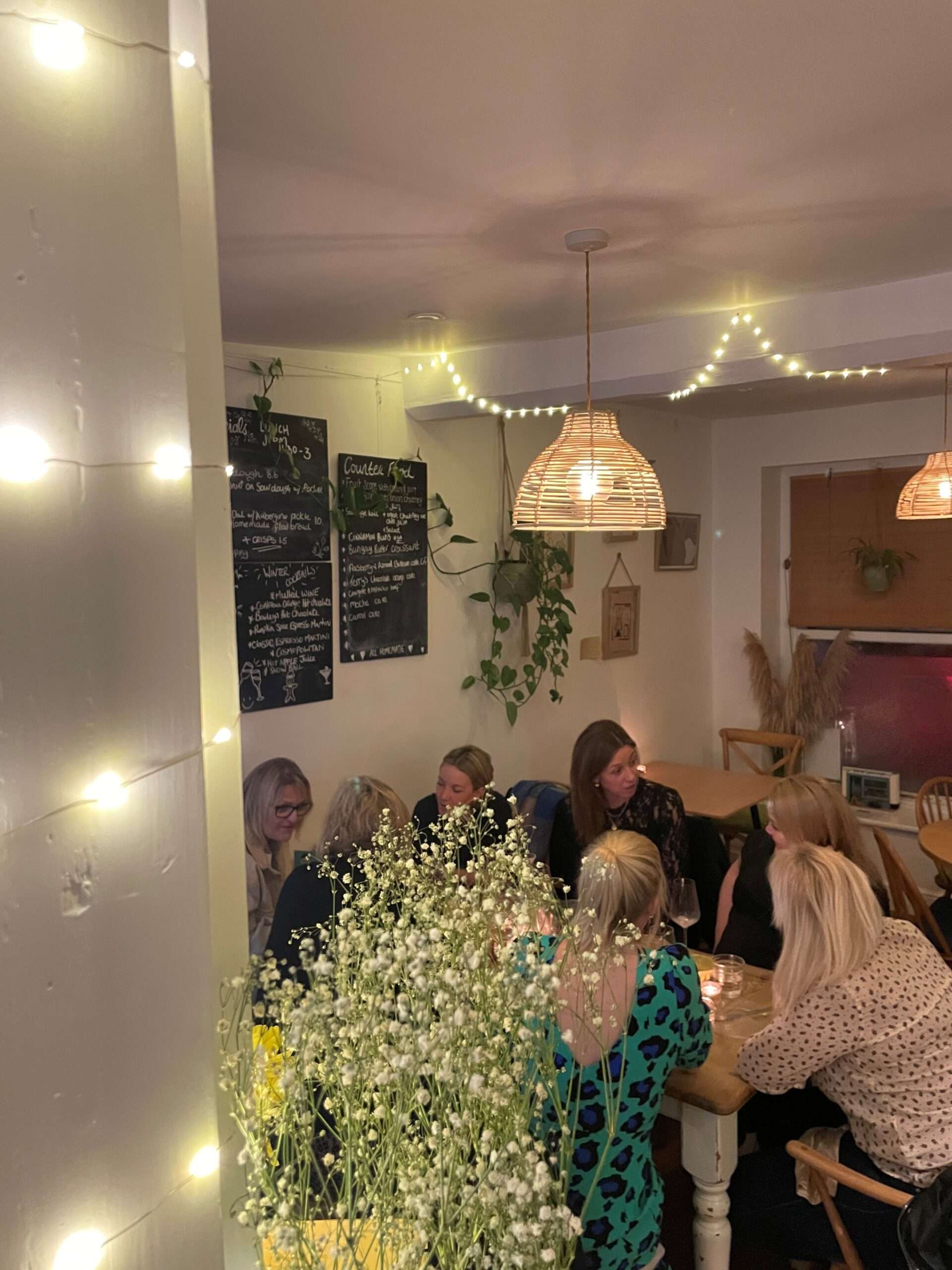 Interior of SOUL Café in Harleston showing customers seated at tables in a cosy café setting, with warm lighting, pendant lamps and decorative fairy lights.
