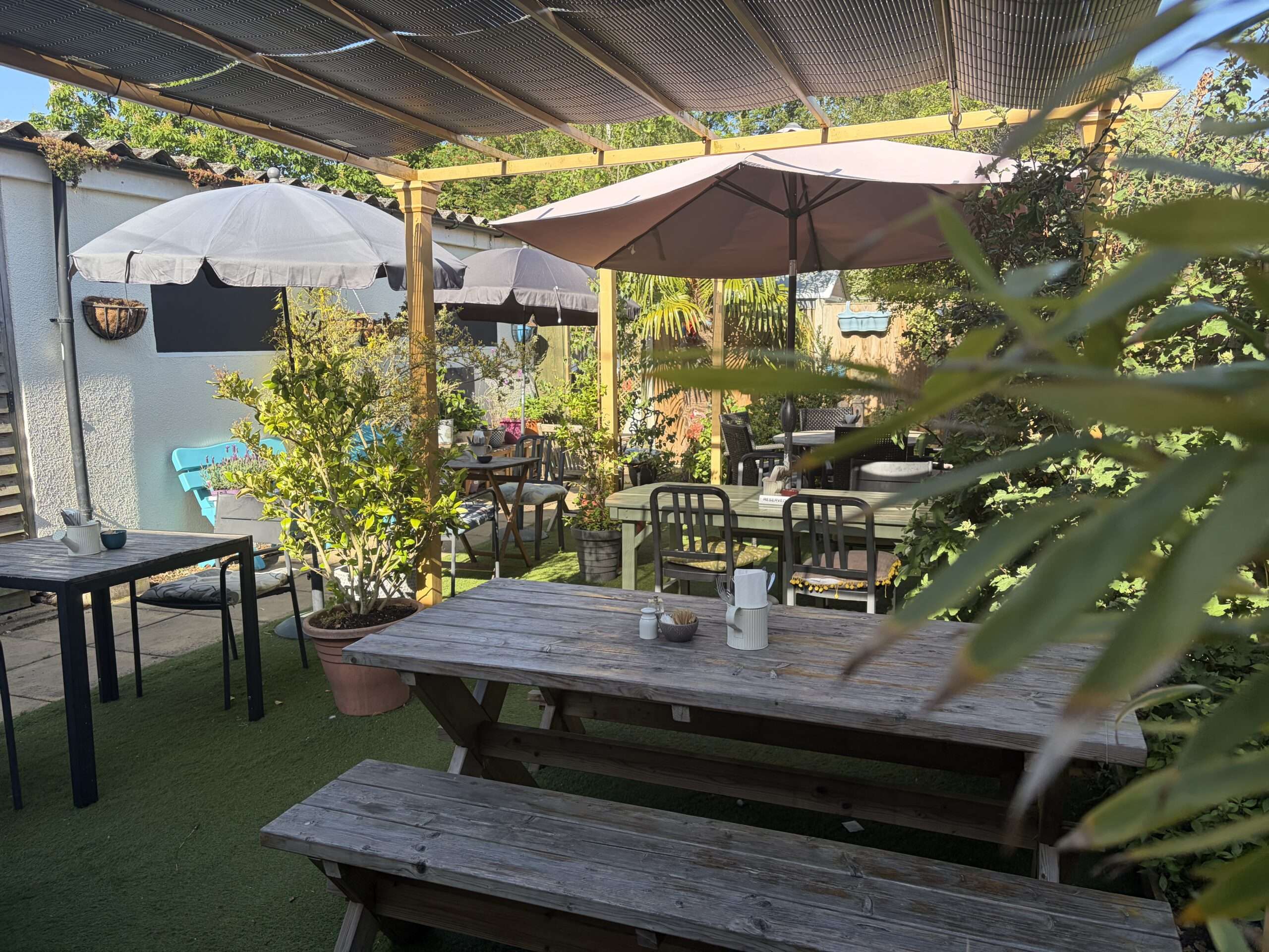 Garden seating area with picnic benches and parasols in a landscaped outdoor setting at Town Green Garden cafe