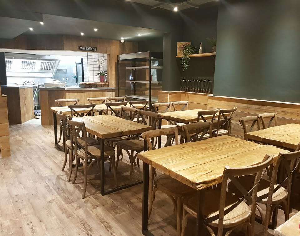 Spacious dining area inside The Hideout featuring wooden tables, chairs and a welcoming café atmosphere.